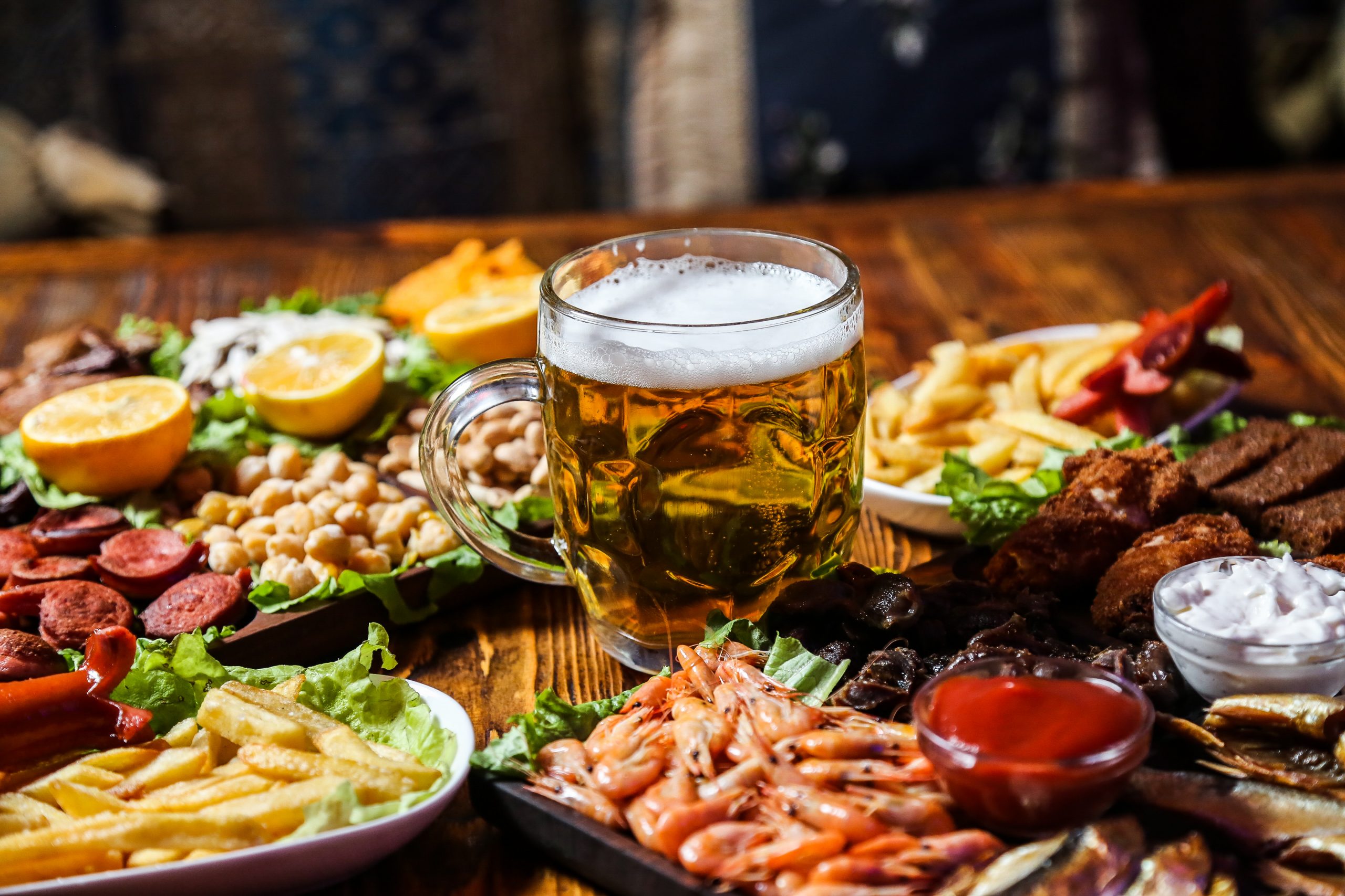 front view beer snacks sausages peas seeds and french fries with lemon wedges on a stand with a glass of beer